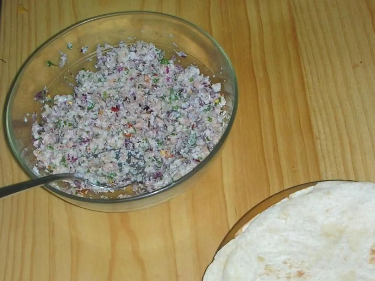 Cuenco de cristal con mas huni, mezcla de atún, coco y cebolla, junto a un pan roshi sobre una mesa de madera