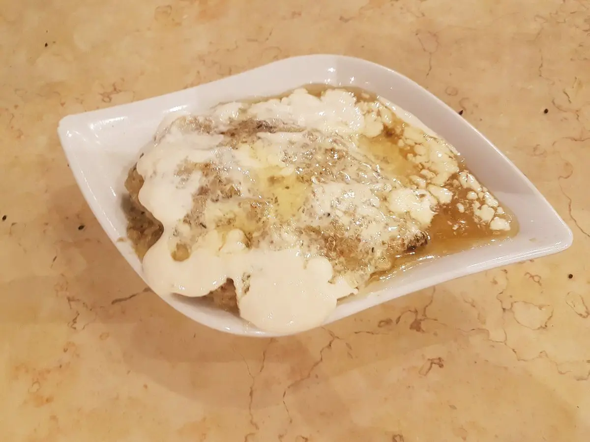 Plato blanco con pan desmenuzado, plátano y crema blanca con miel y especias por encima