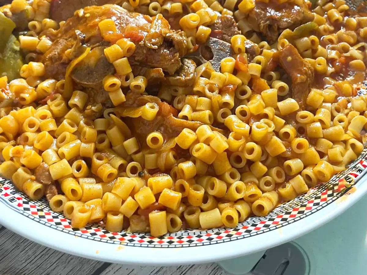 Fuente de pasta corta guisada de color anaranjado con trozos de cordero en salsa de tomate
