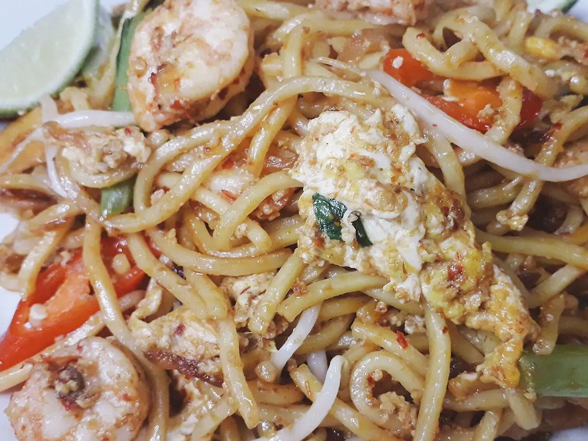 Fideos amarillos fritos con gambas, huevo revuelto, tomate y cebolla en primer plano