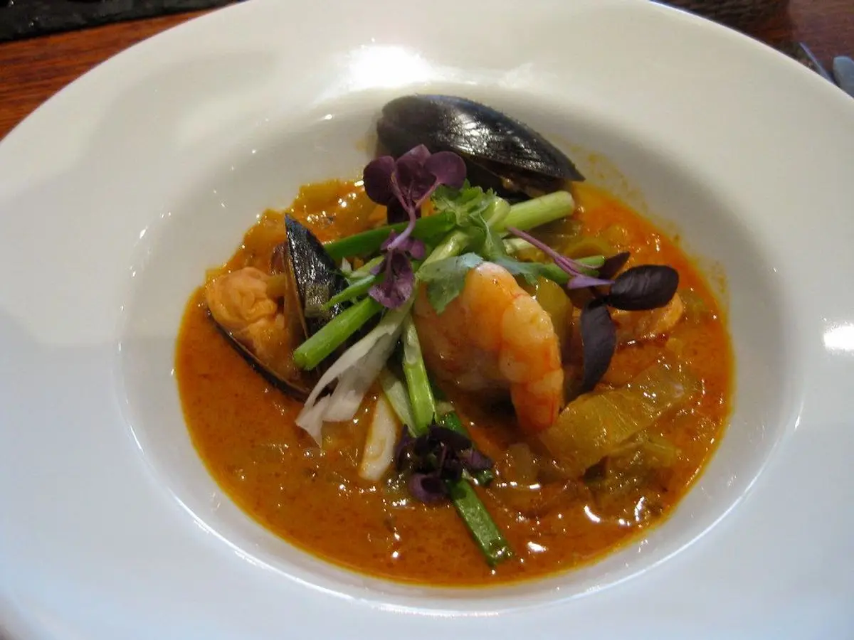 Plato hondo blanco con mejillones, marisco y verdura en salsa naranja de curry