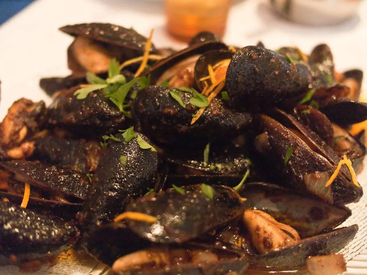 Plato de mejillones en su concha salteados en una salsa picante oscura con tiras de guindilla