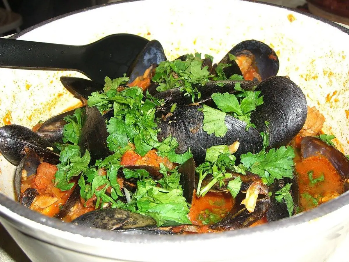 Cazuela blanca con mejillones, perejil picado y zanahoria en trozos