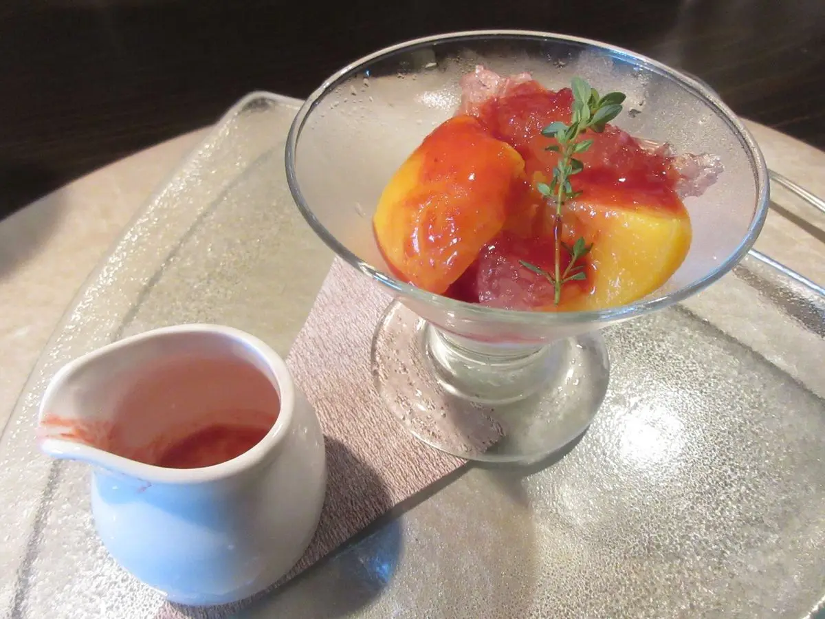 Copa de cristal con melocotón escalfado y salsa de frambuesa, con una jarrita de coulis al lado