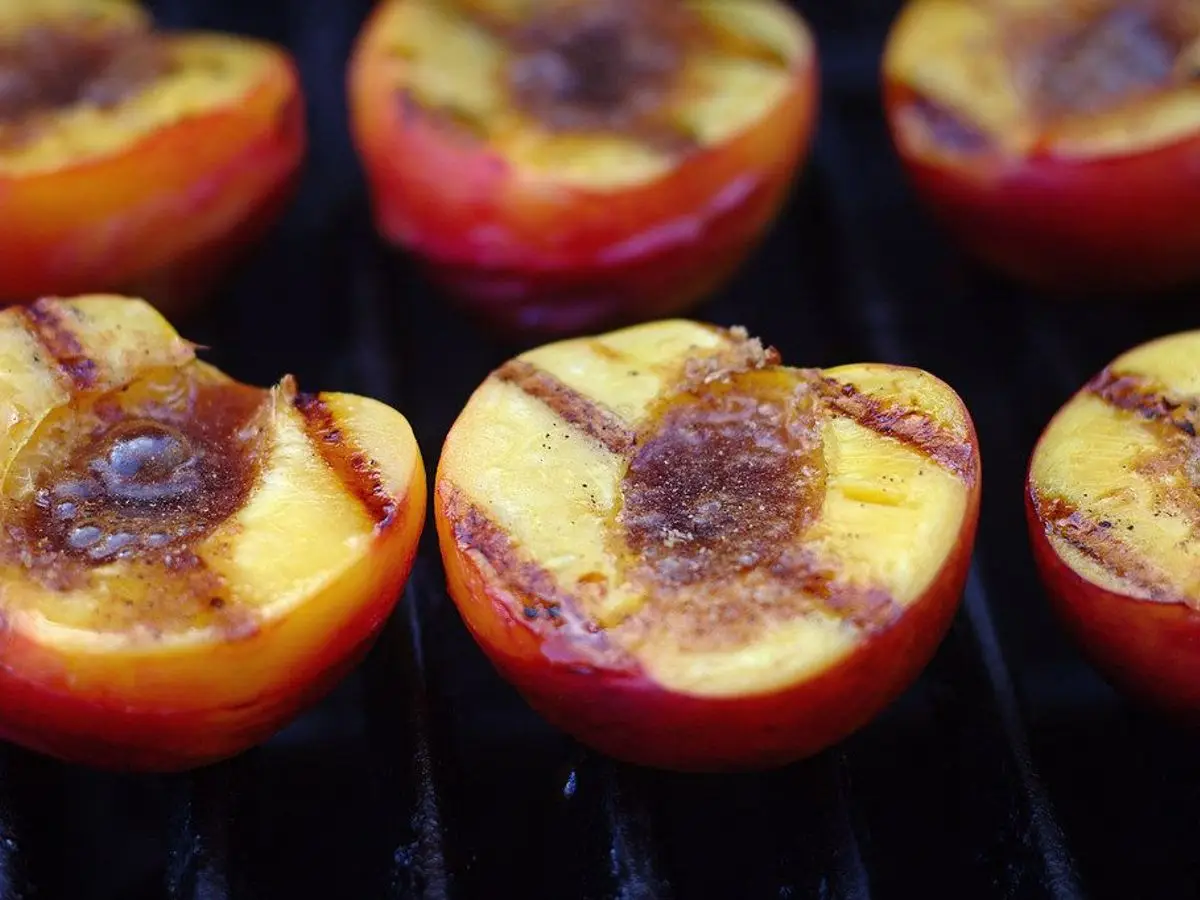 Mitades de melocotón doradas sobre la parrilla, con marcas de brasa