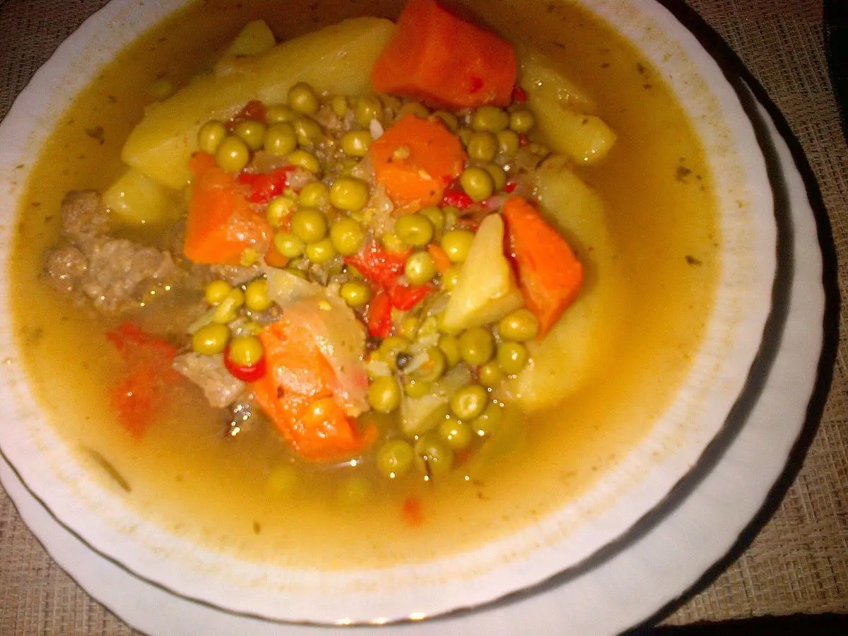 Plato blanco de guiso de carne con guisantes, zanahoria y patata en caldo dorado