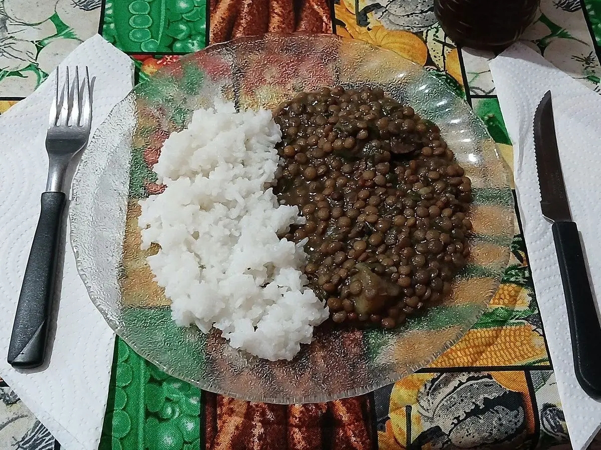 Plato con lentejas guisadas junto a arroz blanco, con tenedor y cuchillo sobre un mantel de colores