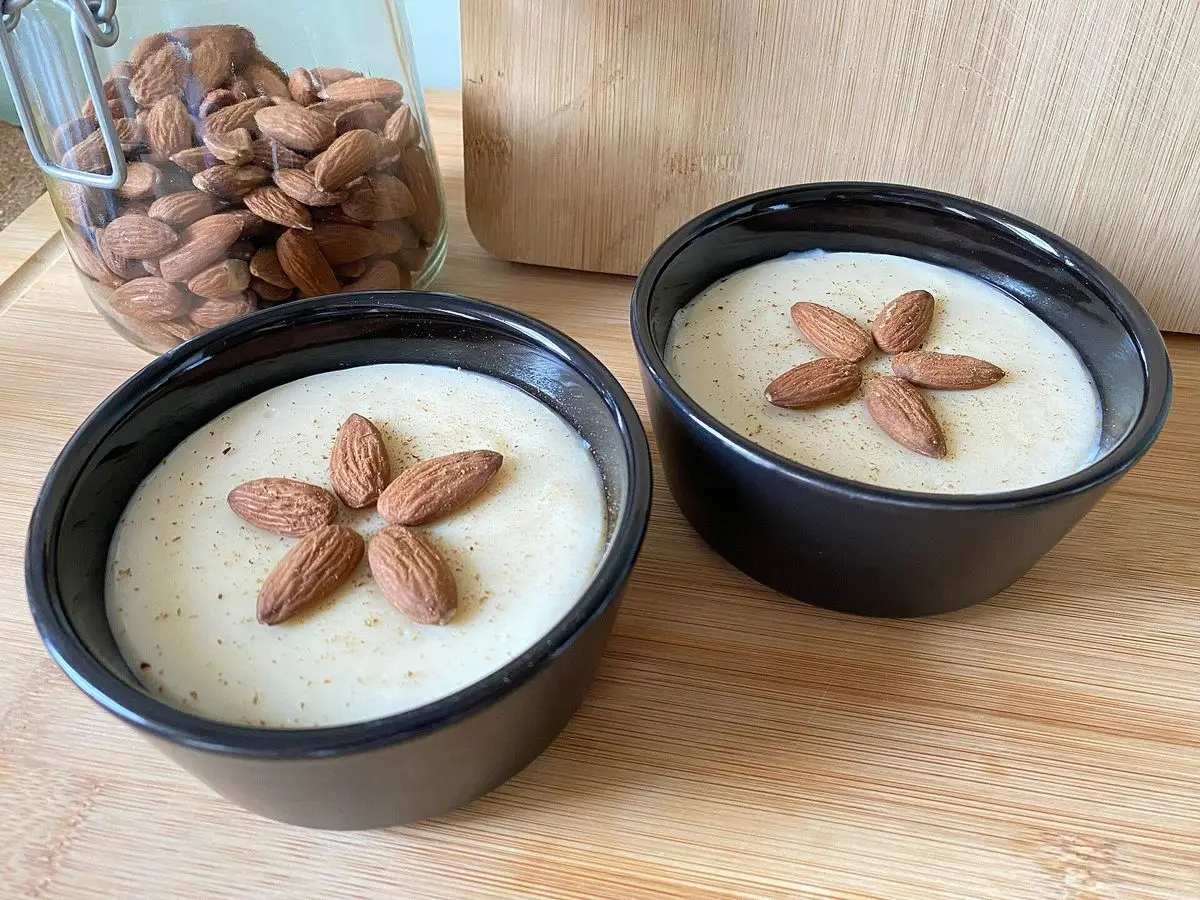Dos cuencos negros de menjar blanc con almendras enteras dispuestas como una flor