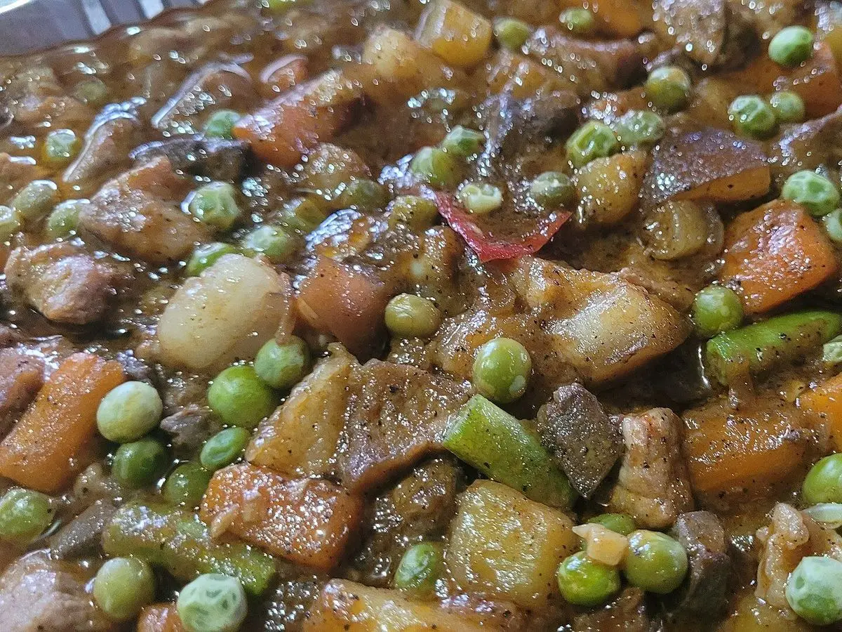 Guiso de cerdo troceado con patata, zanahoria, guisantes y pimiento en salsa roja