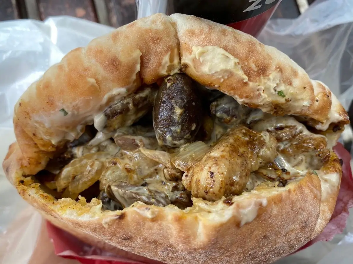 Pan de pita relleno de pollo salteado con menudillos y cebolla, envuelto en papel