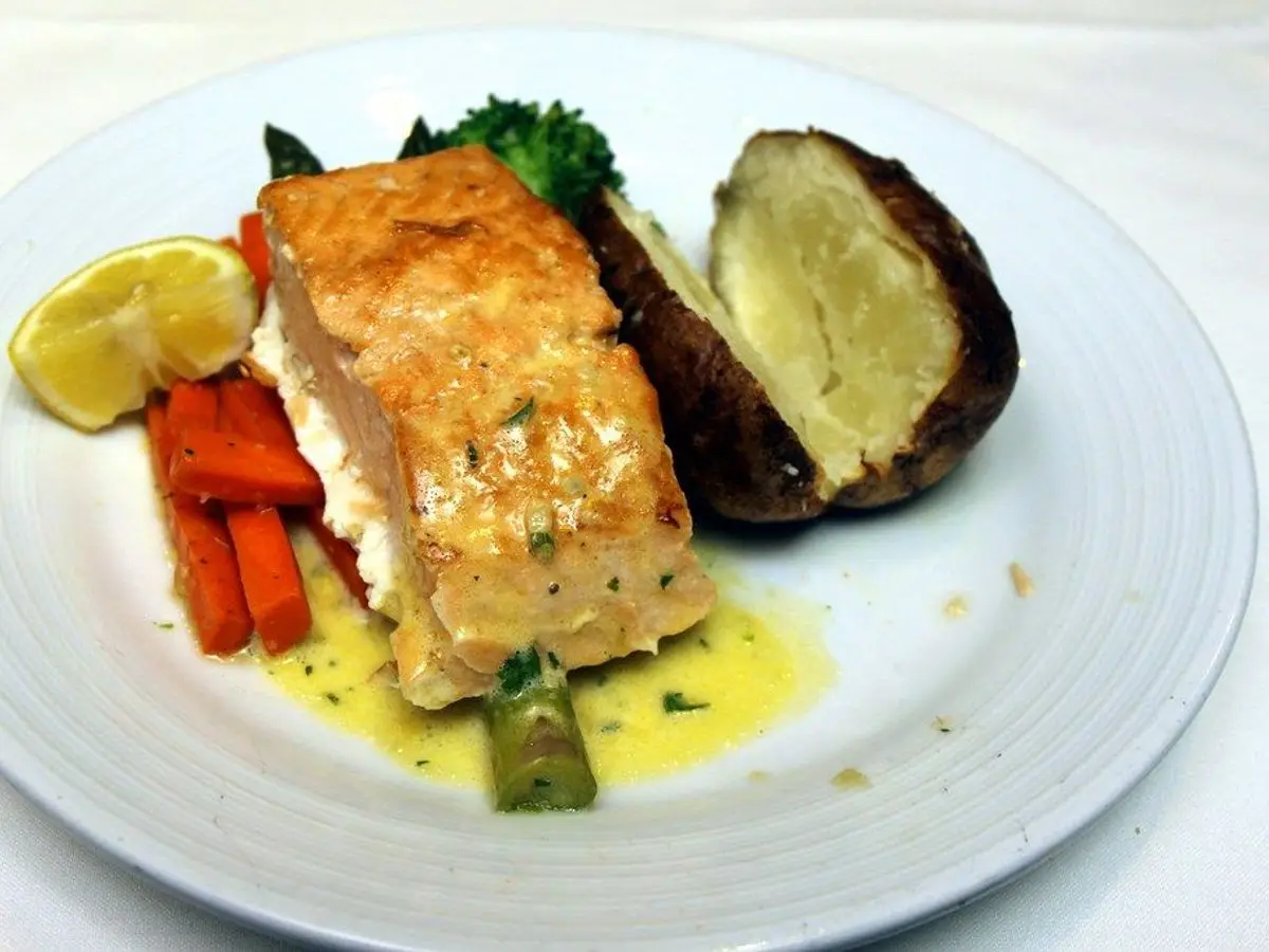 Filete de pescado dorado con patata asada, zanahoria, brócoli y limón en un plato blanco