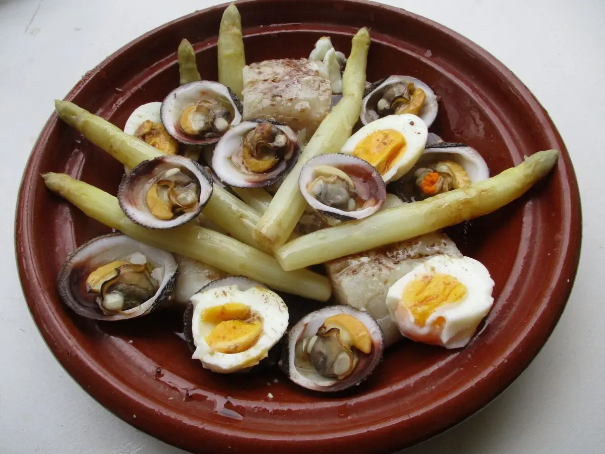 Cazuela de barro con lomos de merluza, almejas abiertas, espárragos blancos y huevos cocidos en mitades