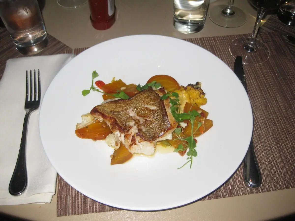Filete de pescado con coliflor asada, remolacha dorada y hierbas frescas en un plato blanco redondo