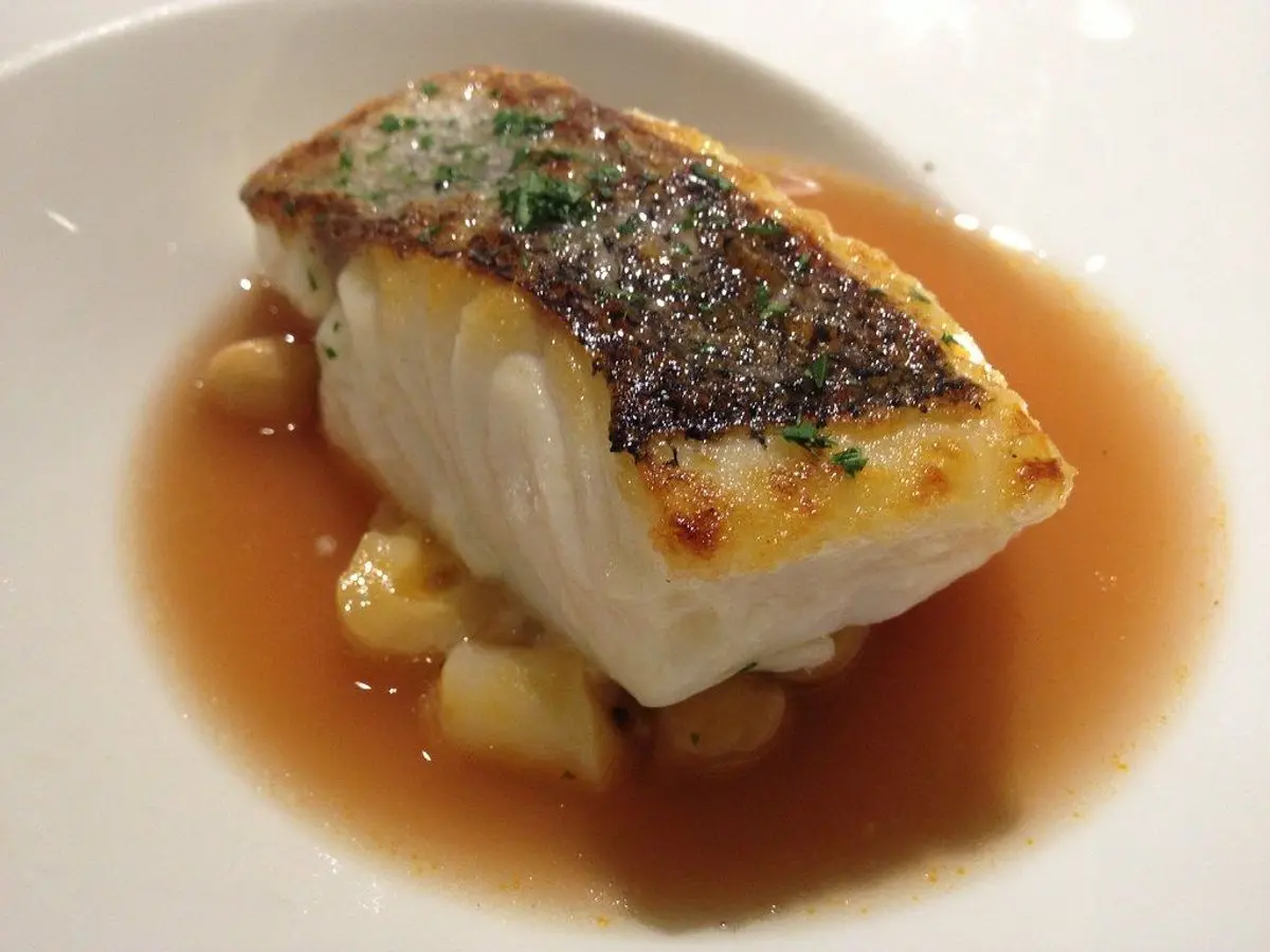 Lomo de merluza dorado en caldo claro con garbanzos en un plato hondo blanco