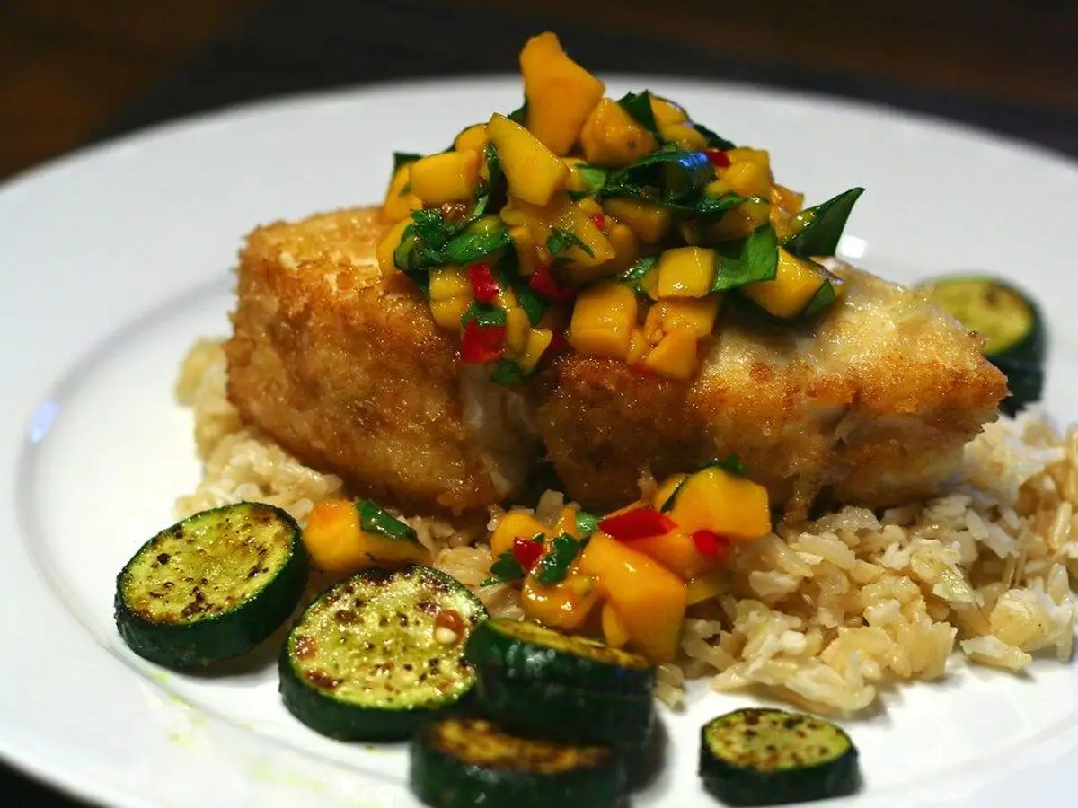 Filete de pescado blanco dorado con salsa de mango sobre arroz de coco, con rodajas de calabacín a la plancha