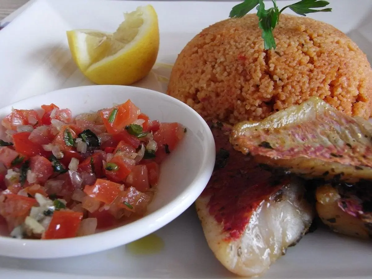 Filete de pescado a la plancha con cuscús y ensalada de tomate picado, junto a una rodaja de limón