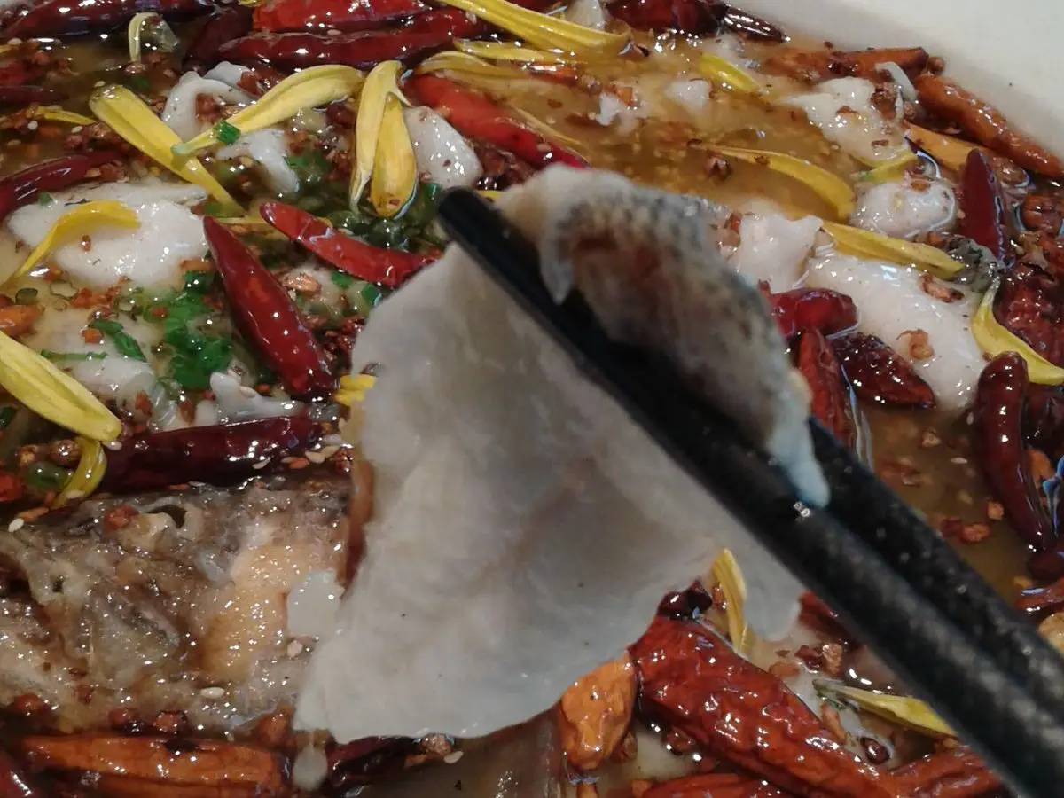 Láminas de pescado blanco cocido en caldo con guindillas rojas y flores, levantadas con palillos