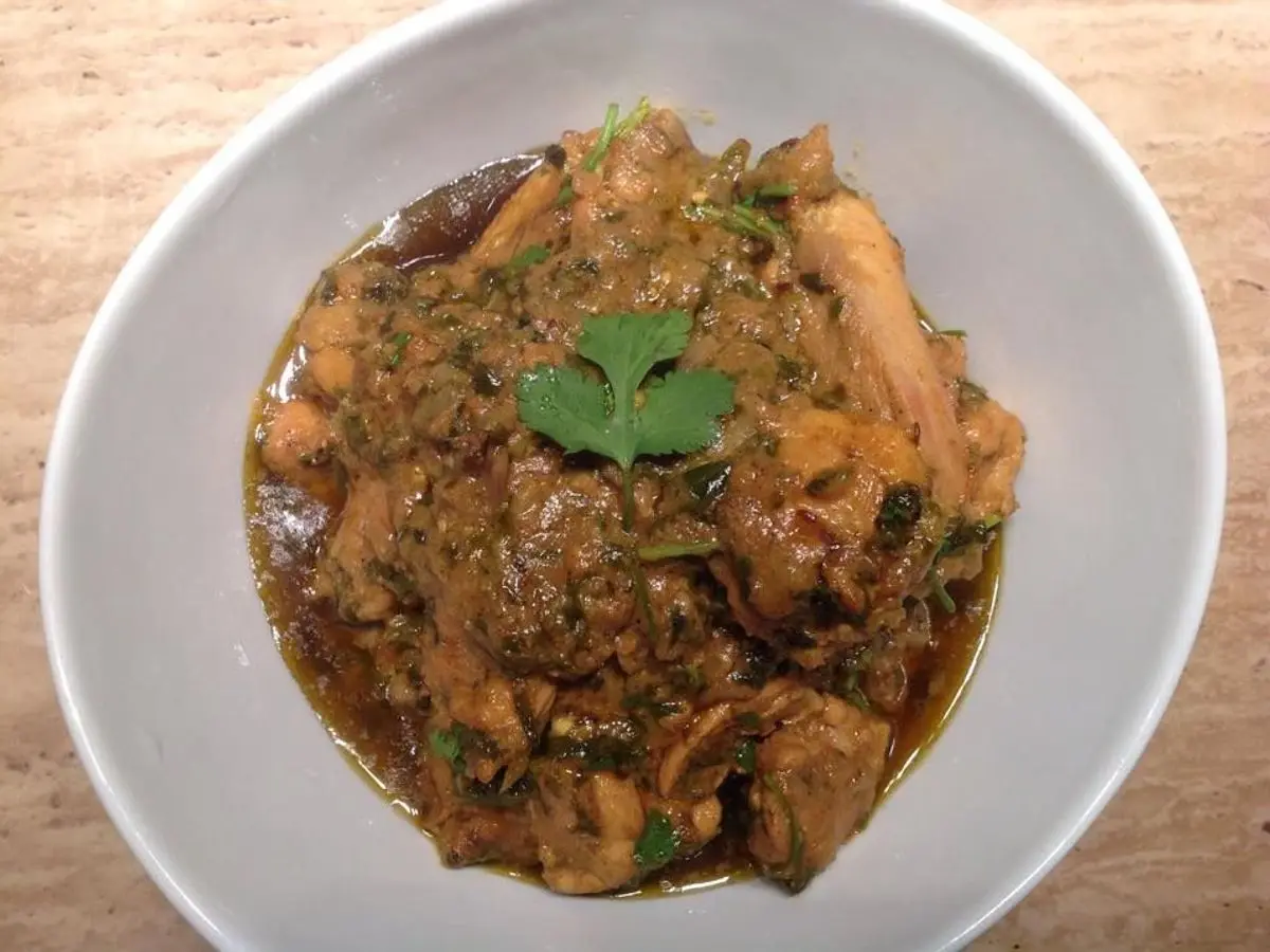 Cuenco blanco de pollo guisado con hojas verdes de fenogreco en salsa especiada oscura