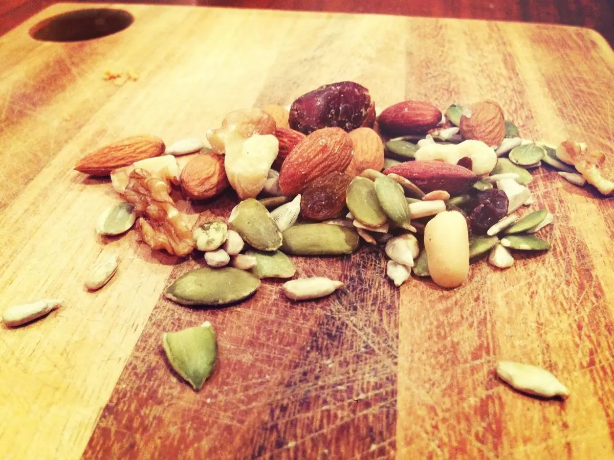 Mezcla de frutos secos, almendras, pipas y fruta deshidratada esparcidas sobre una tabla de madera