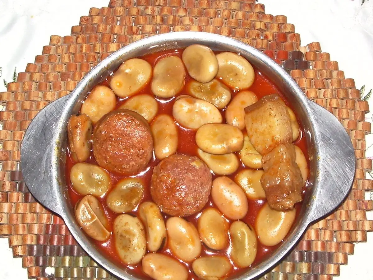 Cazuela de habas guisadas con rodajas de chorizo en salsa roja sobre una trébede de mimbre