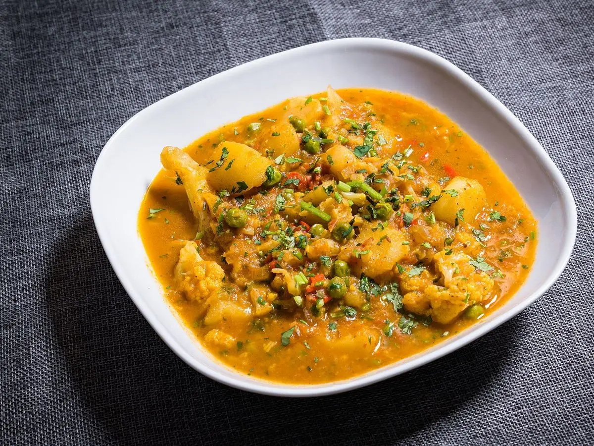 Cuenco blanco de curry anaranjado con coliflor y patata sobre un mantel gris