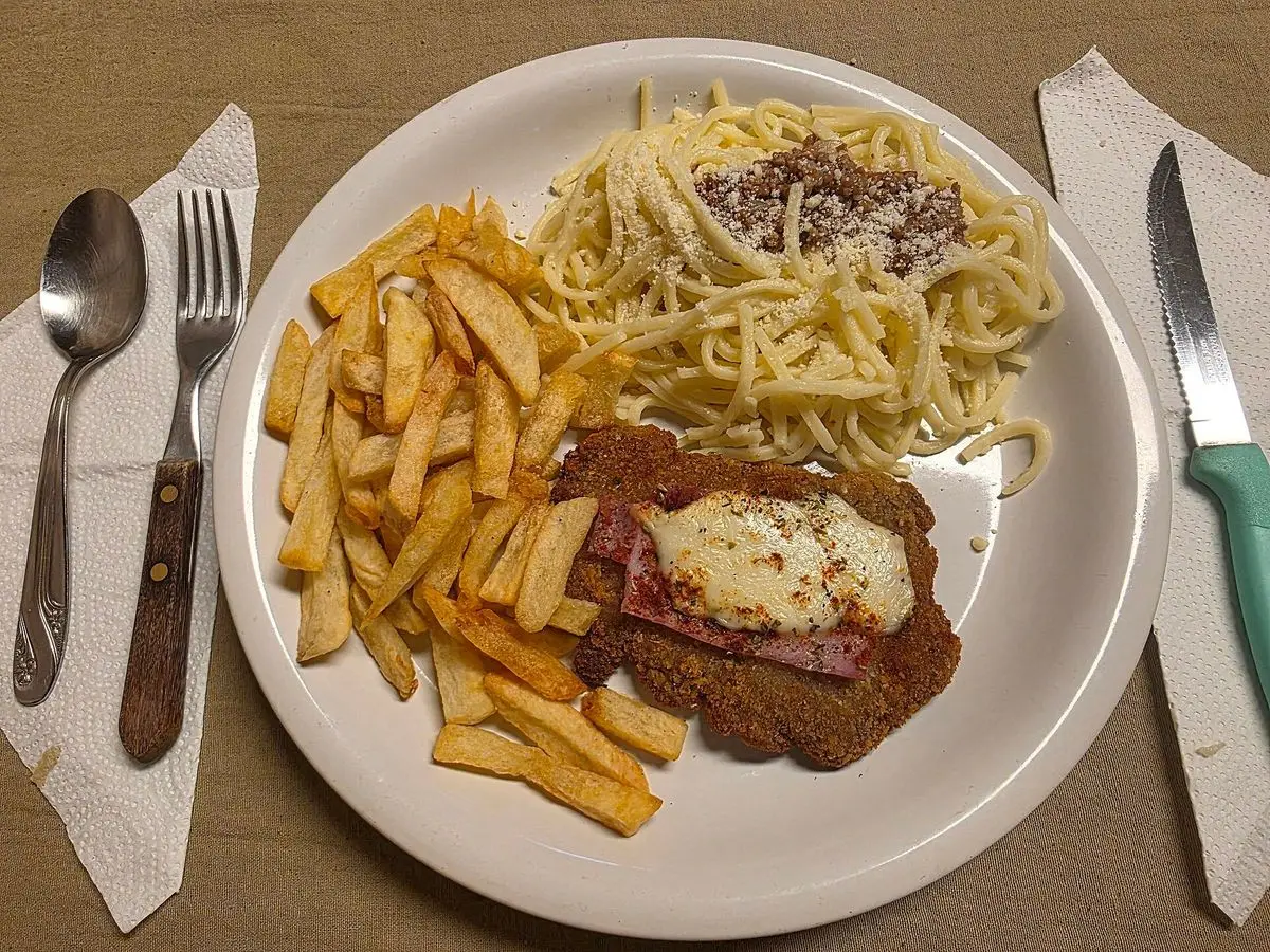 Milanesa a la napolitana con jamón y queso gratinado, patatas fritas y espaguetis en un plato blanco