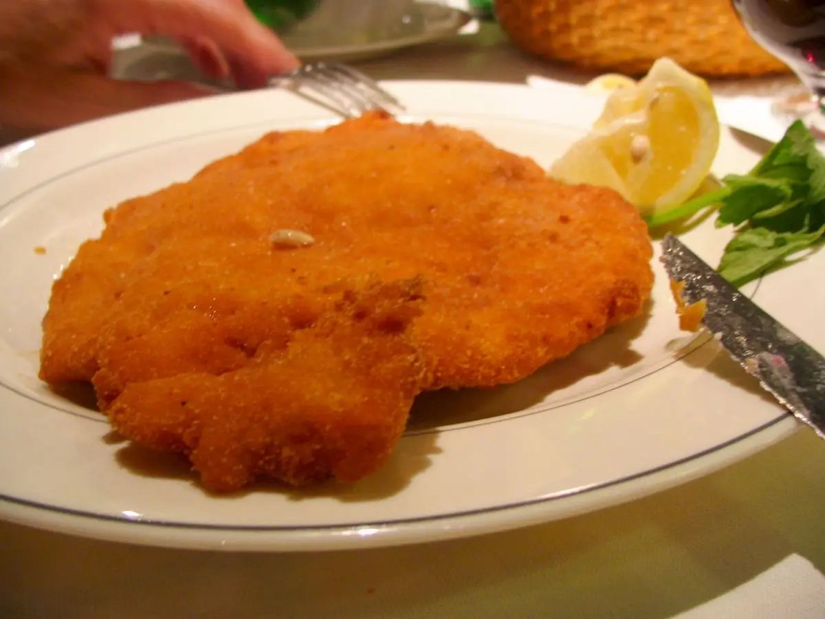Milanesa empanada dorada en un plato con rodaja de limón y ensalada verde