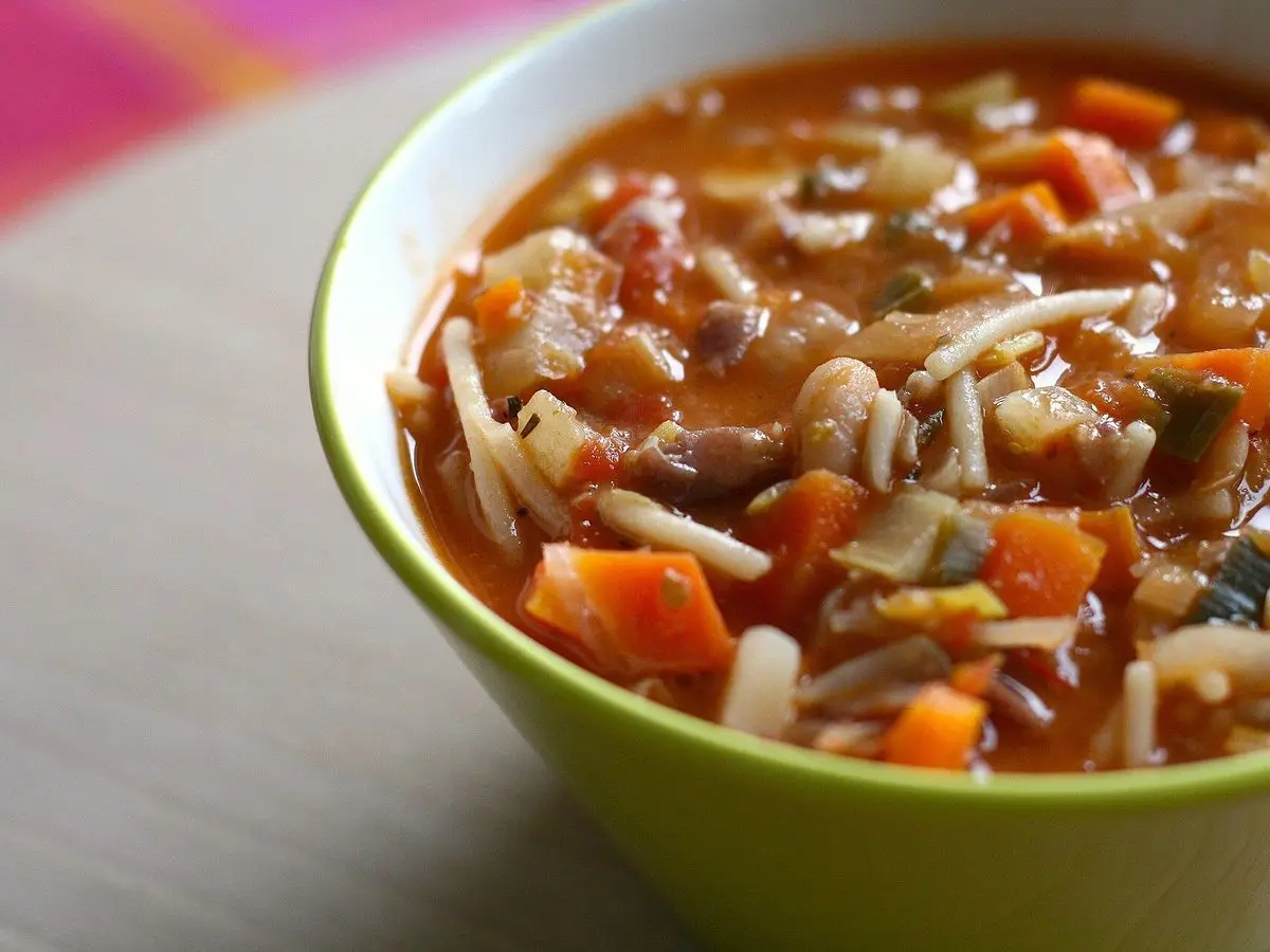 Cuenco verde de sopa minestrone con zanahoria, pasta y verduras en caldo de tomate