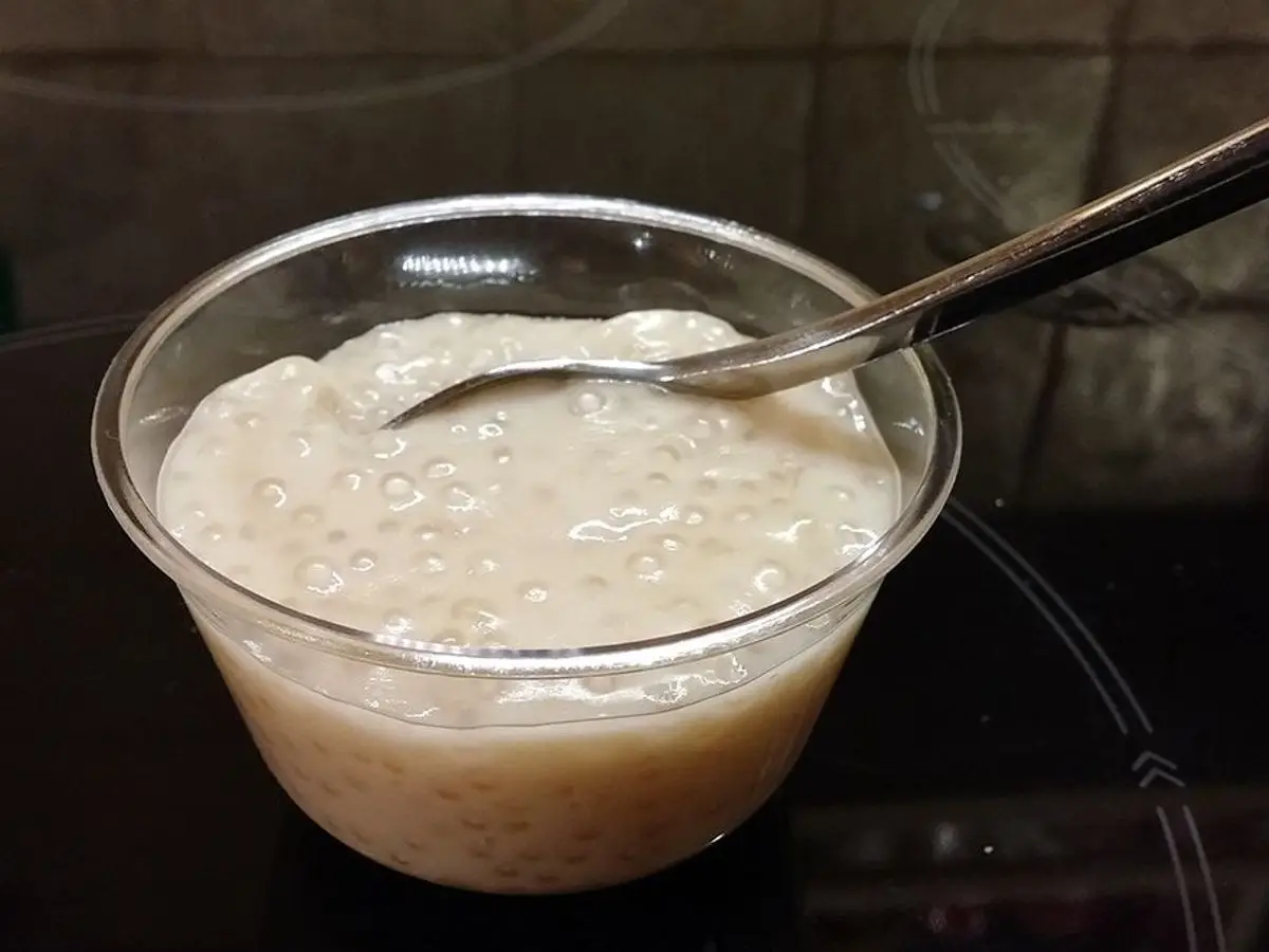 Vasito transparente de pudin cremoso de tapioca con una cuchara, sobre una superficie oscura