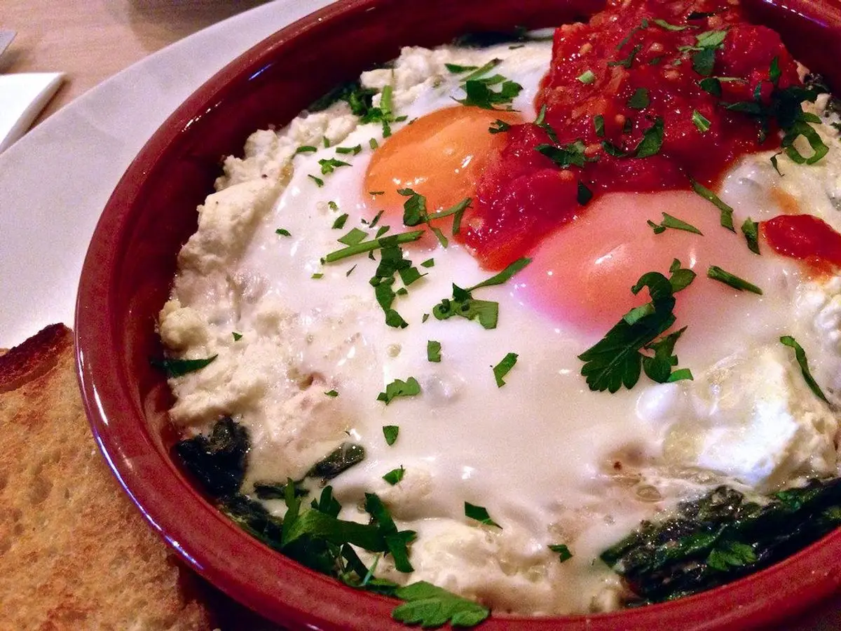 Cazuela de barro con huevos al horno, espinacas, queso feta y tomate picado, con pan