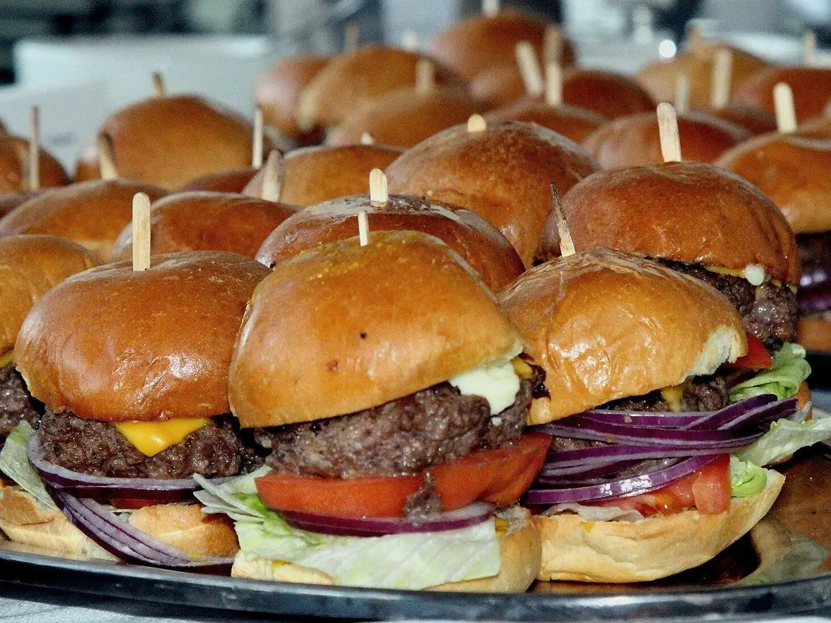Muchas mini hamburguesas con tomate y cebolla morada y palillos en una bandeja