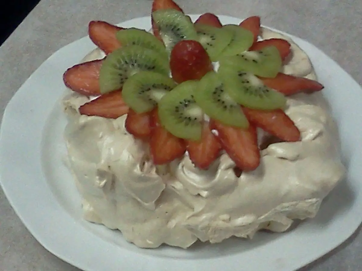 Pavlova de merengue con crema decorada con rodajas de kiwi y fresas sobre un plato blanco