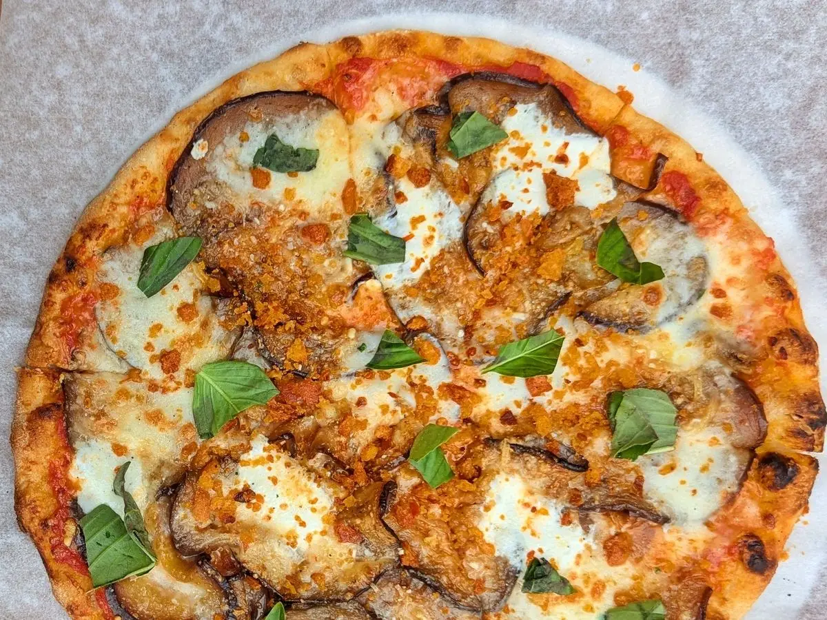 Pizza redonda con rodajas de berenjena asada, mozzarella y hojas de albahaca