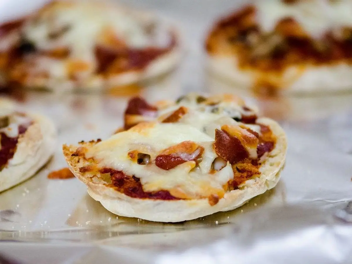 Varias mini pizzas redondas con tomate y queso fundido sobre papel de aluminio