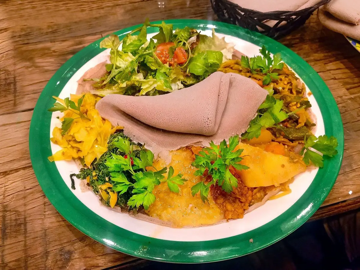 Plato etíope vegetariano con injera, legumbres amarillas y verduras de hoja en un plato verde y blanco