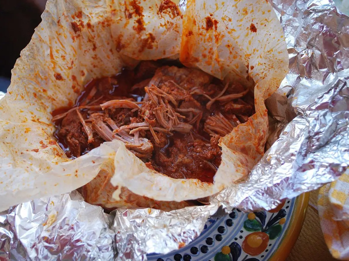 Mixiote abierto con carne deshebrada en adobo rojo dentro del papel y papel de aluminio