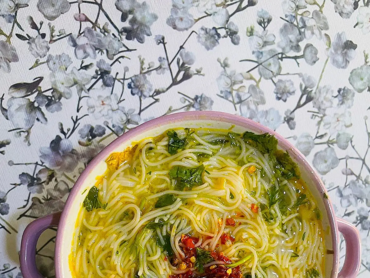 Cuenco de sopa de fideos de arroz finos en caldo amarillo con hierbas y chile por encima