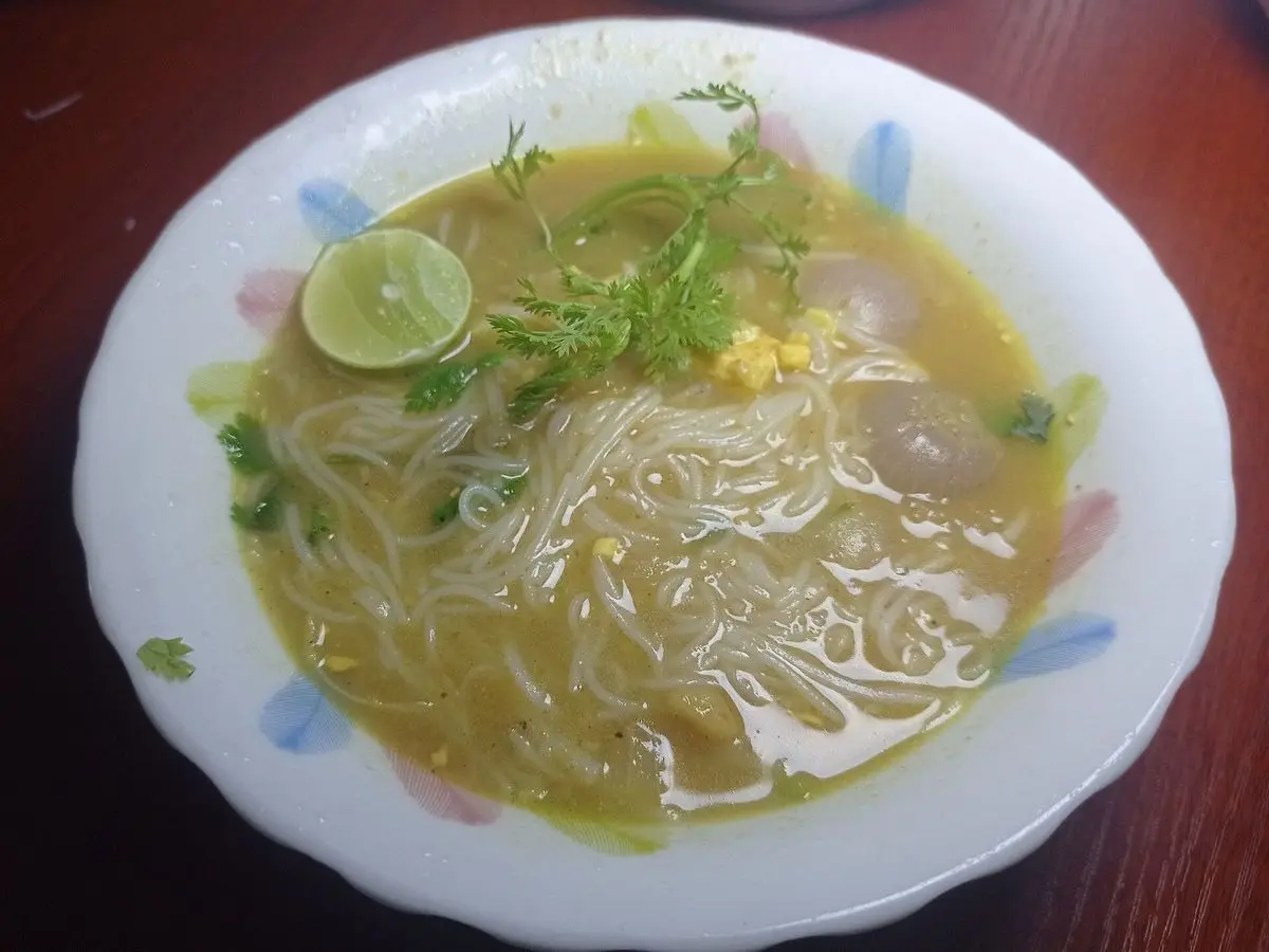 Plato hondo de sopa de fideos de arroz en caldo de pescado con hierbas frescas y media lima