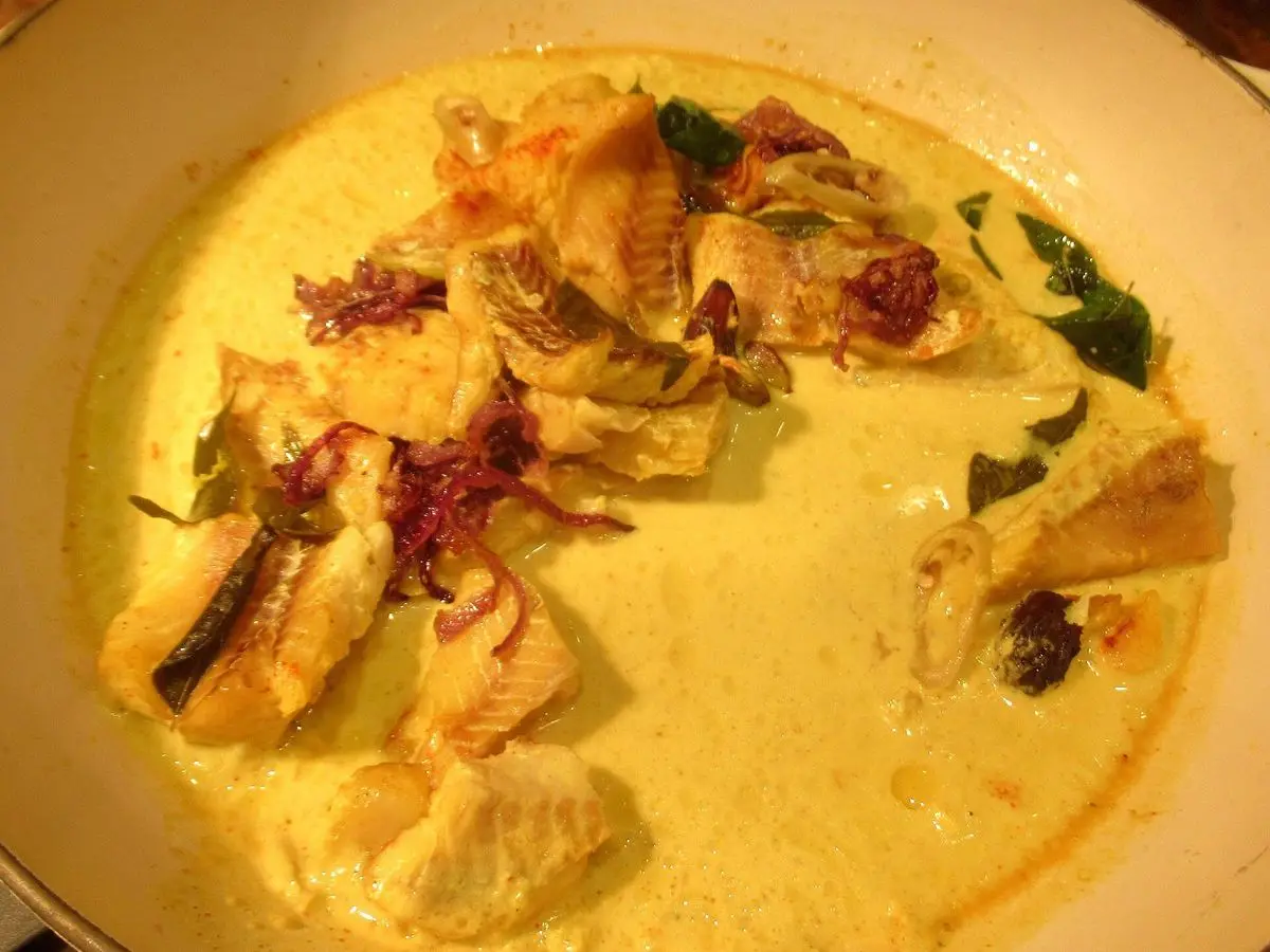 Plato de pescado en salsa cremosa amarilla de coco y cúrcuma con hojas de curry