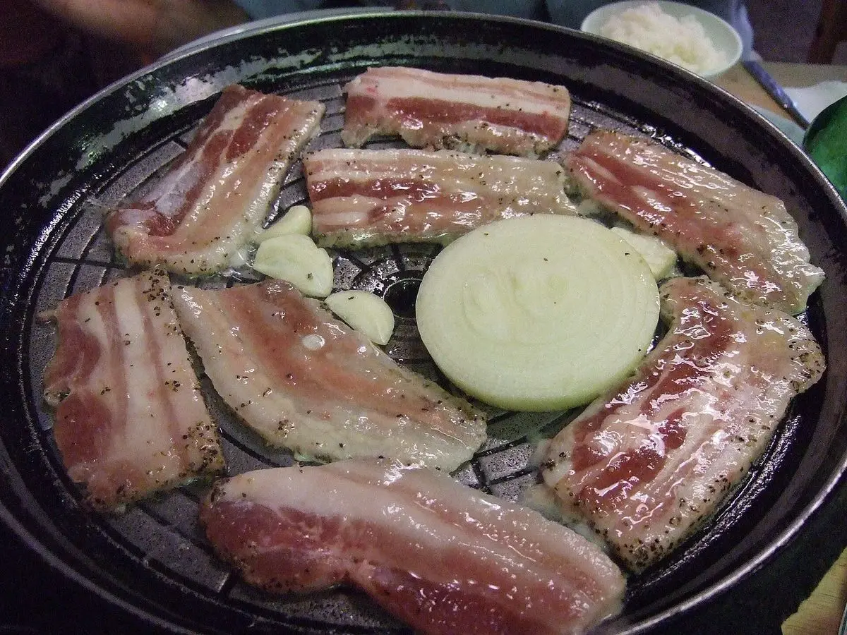 Lonchas de cerdo asadas a la parrilla coreana con cebolla y ajo sobre una plancha redonda