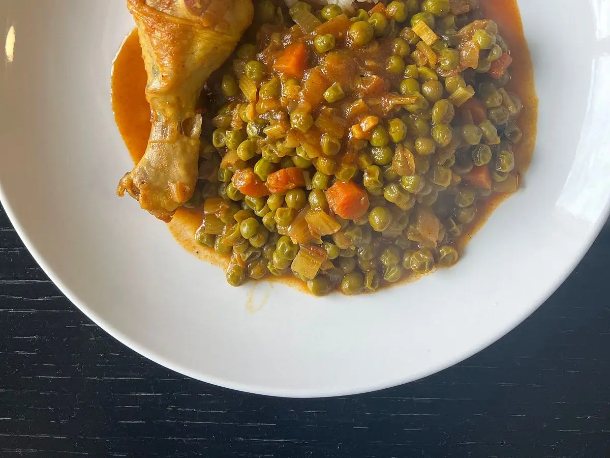 Plato con muslo de pollo y guiso de guisantes con zanahoria en salsa de tomate, con arroz