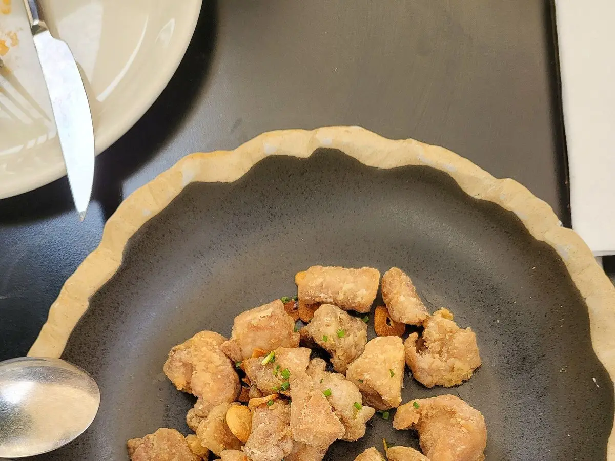 Mollejas de ternera troceadas y doradas en una sartén oscura con un tenedor al lado