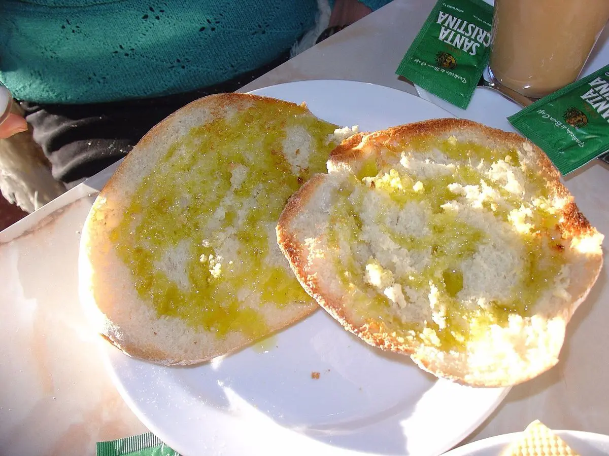 Mollete abierto en dos mitades tostadas con aceite de oliva extendido, sobre un plato blanco