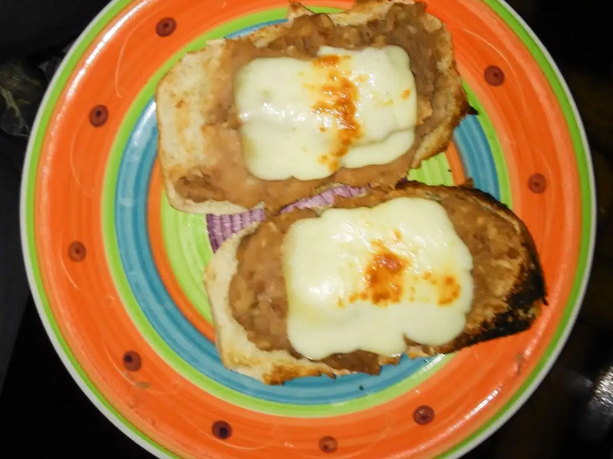 Dos rebanadas de pan tostado con queso fundido sobre un plato de colores