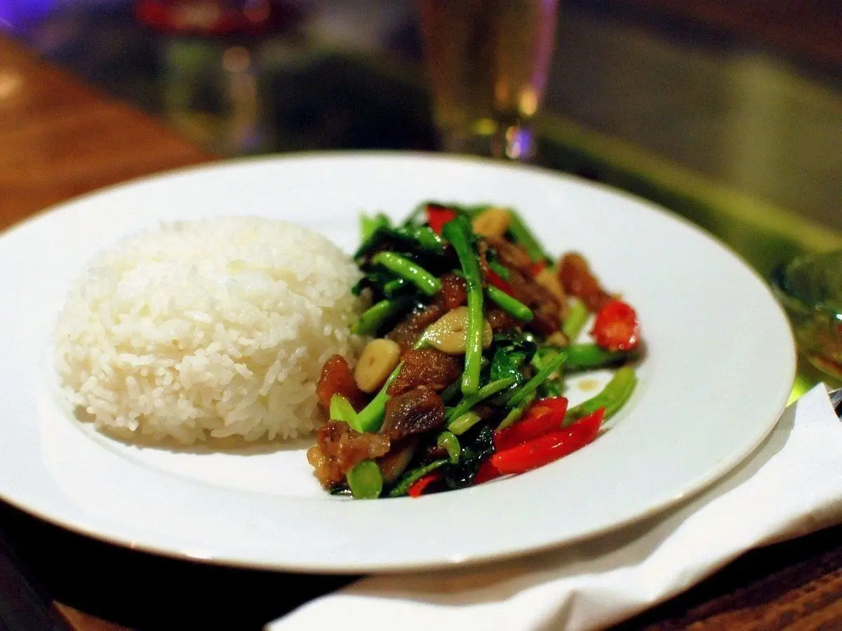 Plato blanco con arroz blanco y cerdo salteado con verdura de hoja verde y guindilla roja