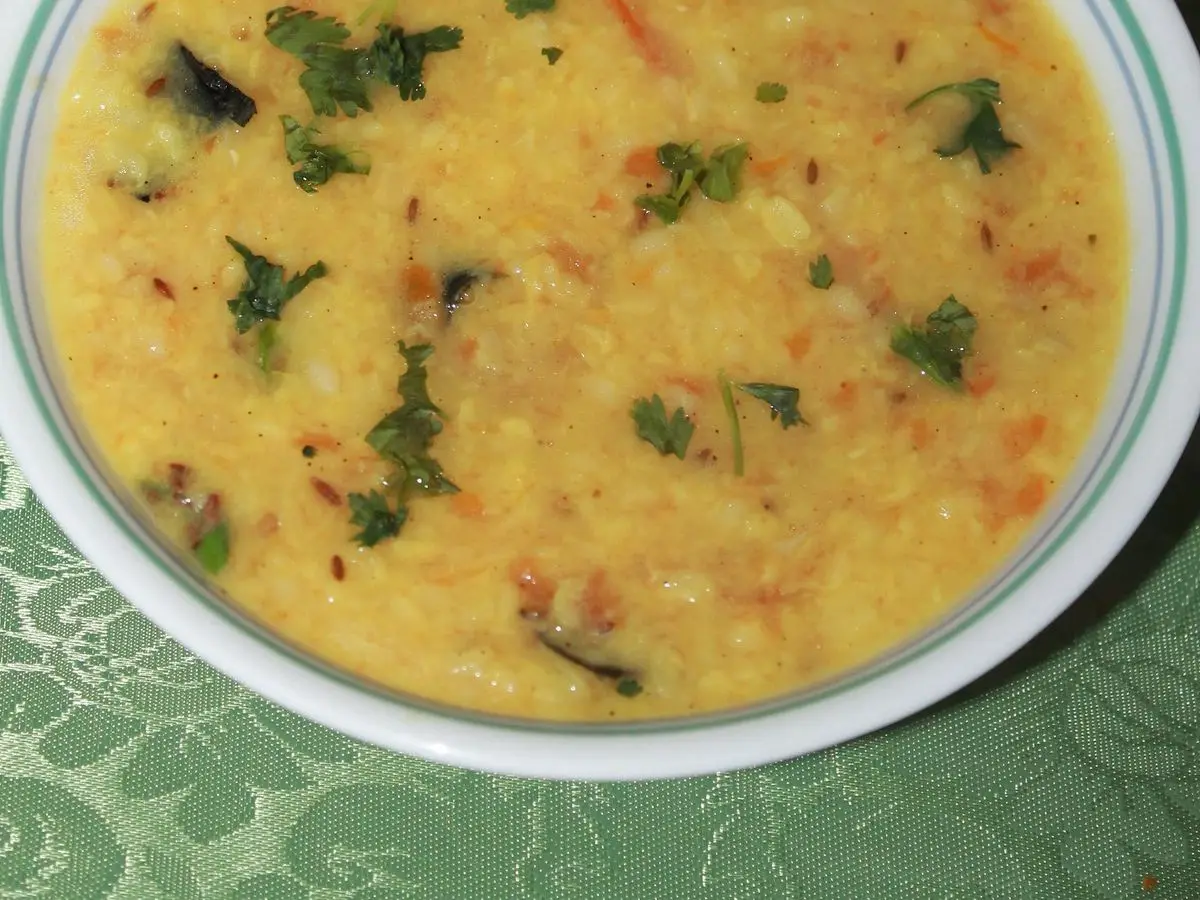 Plato hondo de dal amarillo cremoso de lentejas con hierbas verdes y tomate picado por encima