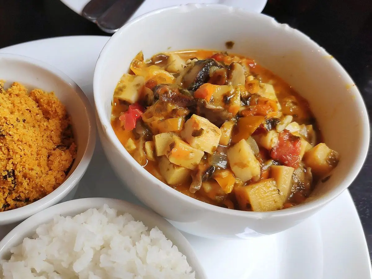 Cuenco de moqueca vegetal con dados de palmito y tomate junto a farofa y arroz blanco