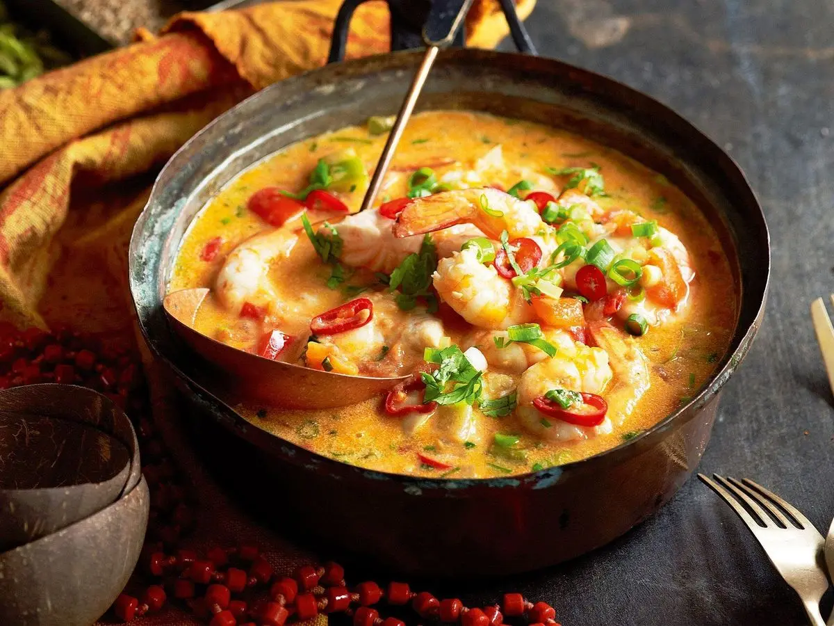 Guiso brasileño de pescado y gambas en salsa cremosa de coco con pimiento y cilantro en una cazuela oscura