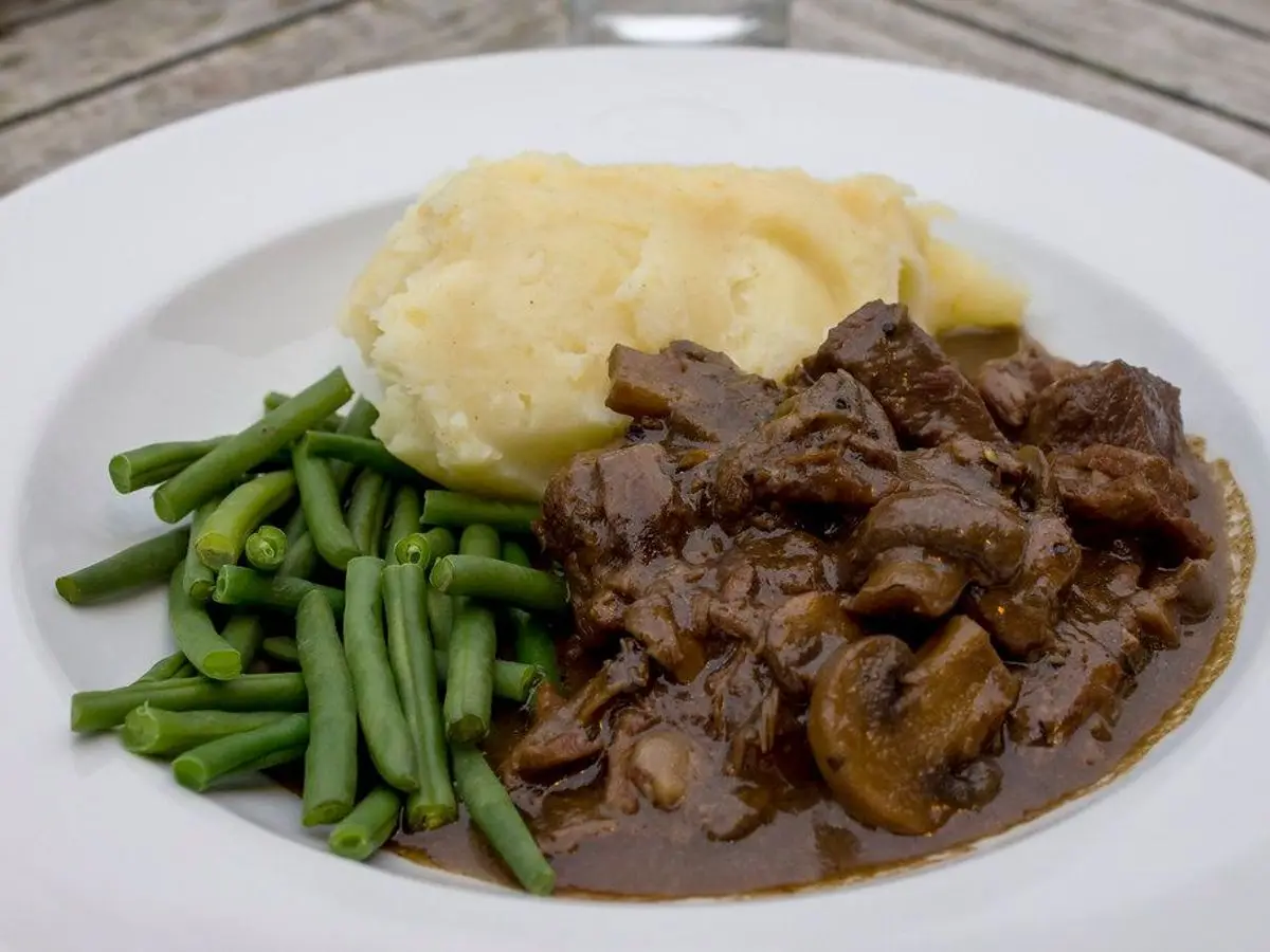 Ternera guisada en salsa oscura con puré de patata y judías verdes en un plato blanco