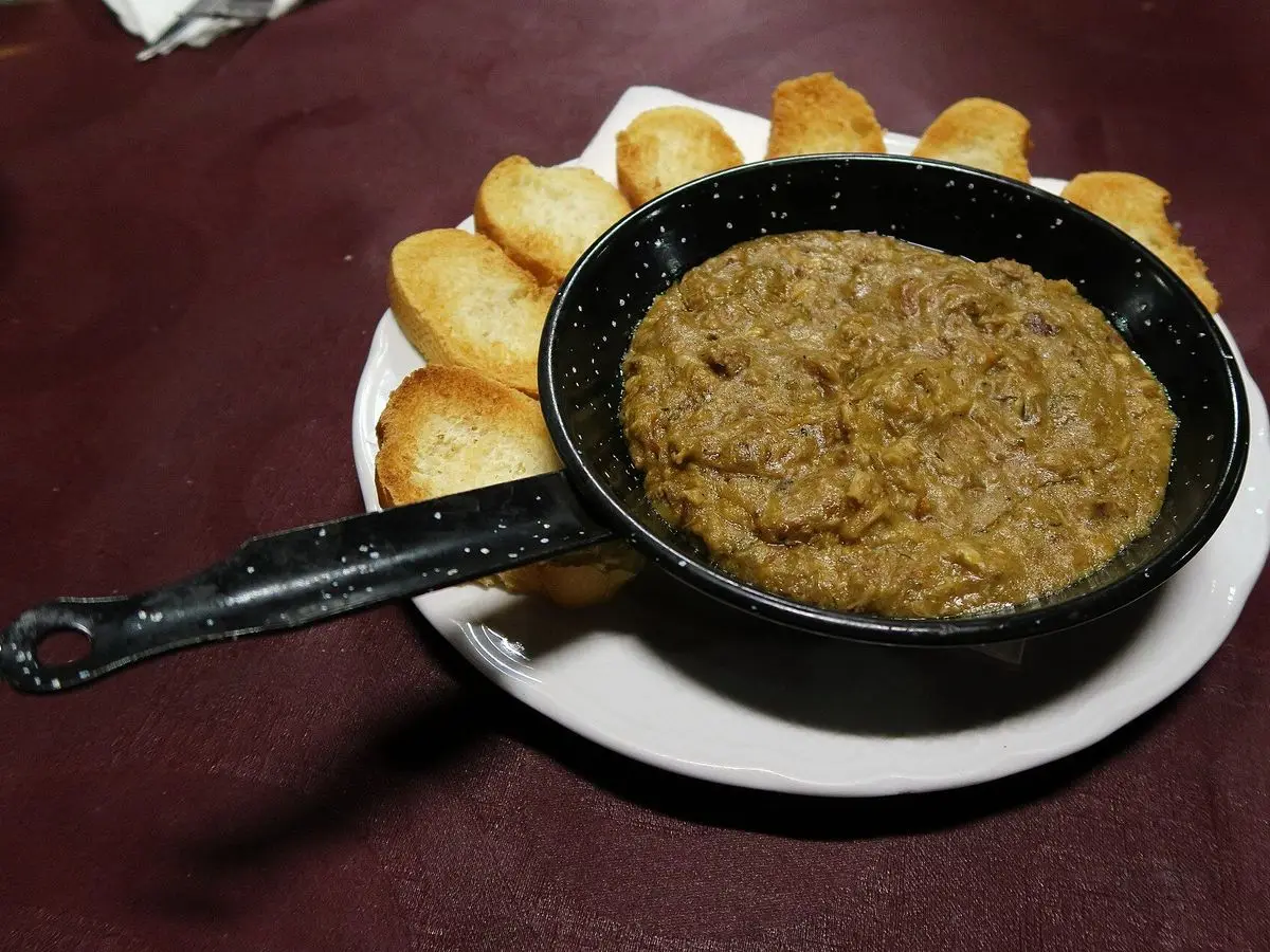 Sartén pequeña con morteruelo conquense rodeada de tostas de pan en un plato blanco